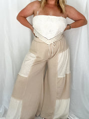 Woman wearing a strapless top and wide-leg pants against a white curtain background