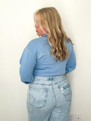 Person wearing a blue jacket and jeans against a white wall.