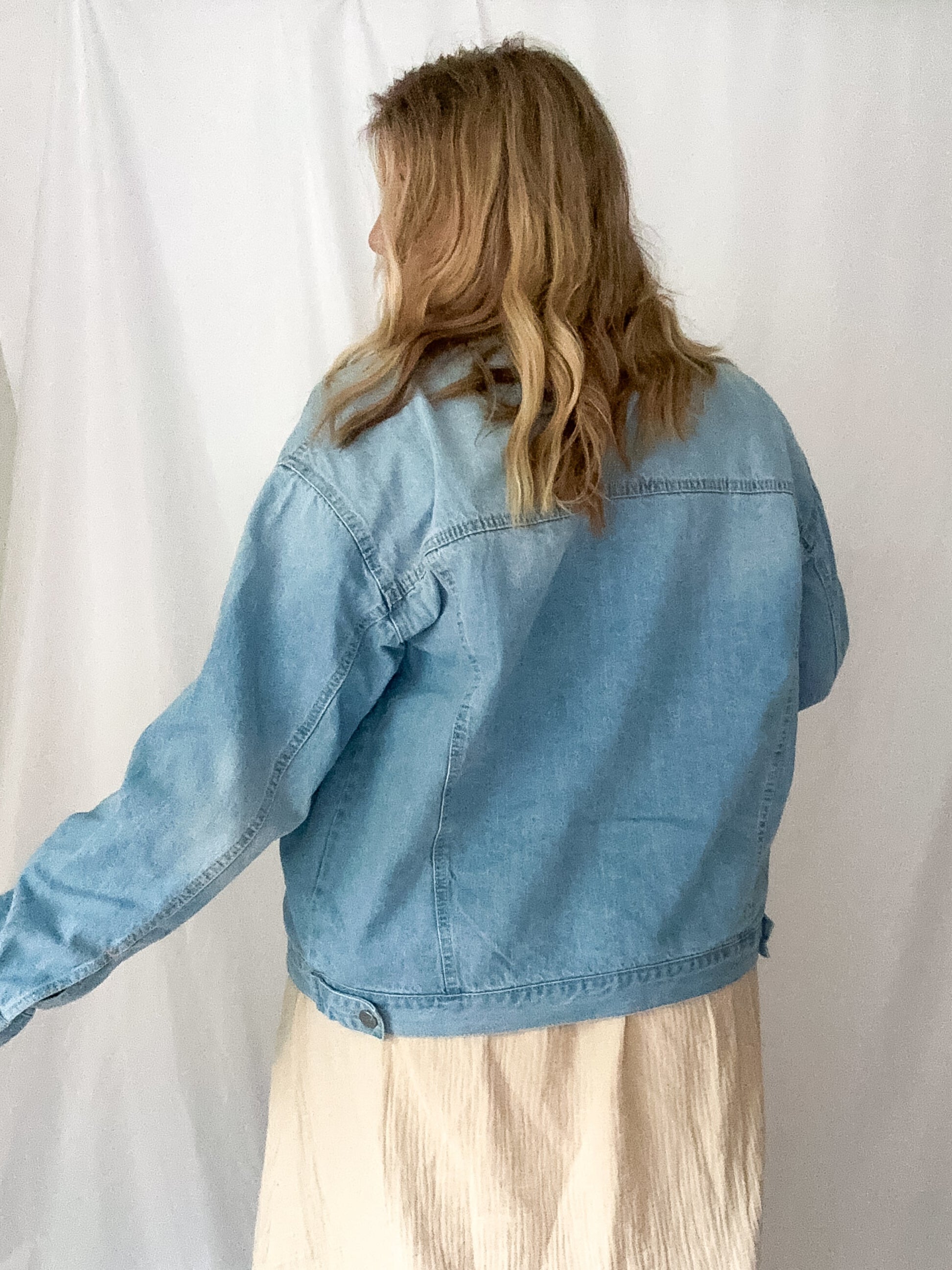 Person wearing a light blue denim jacket against a white background