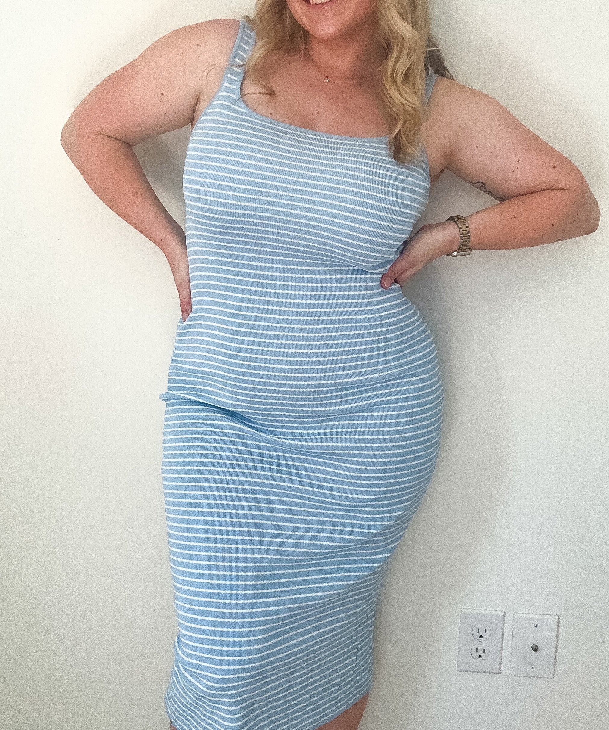 Woman wearing a light blue striped dress against a white wall.