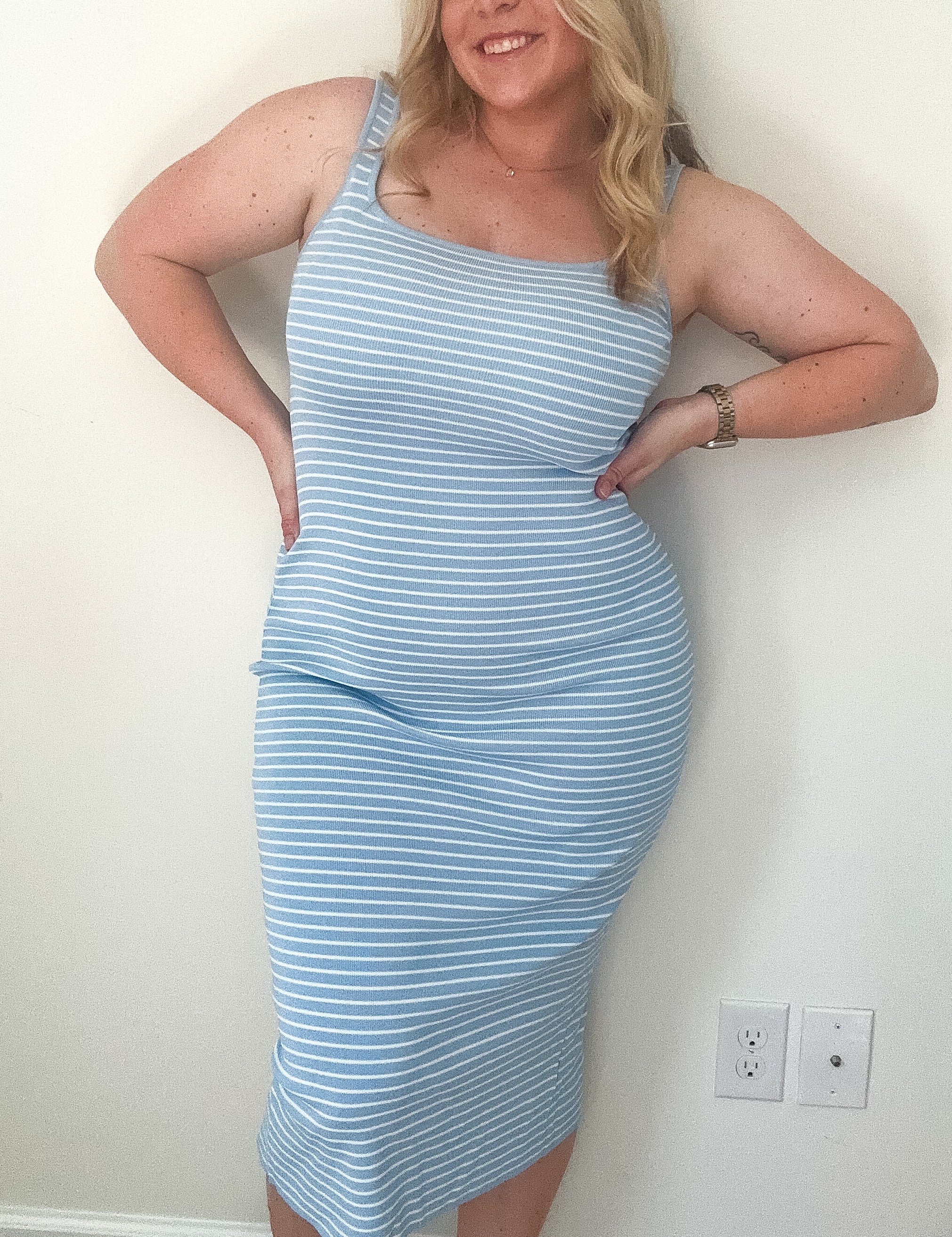 Woman wearing a light blue striped dress against a white wall.