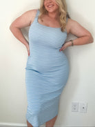 Woman wearing a light blue striped dress against a white wall.