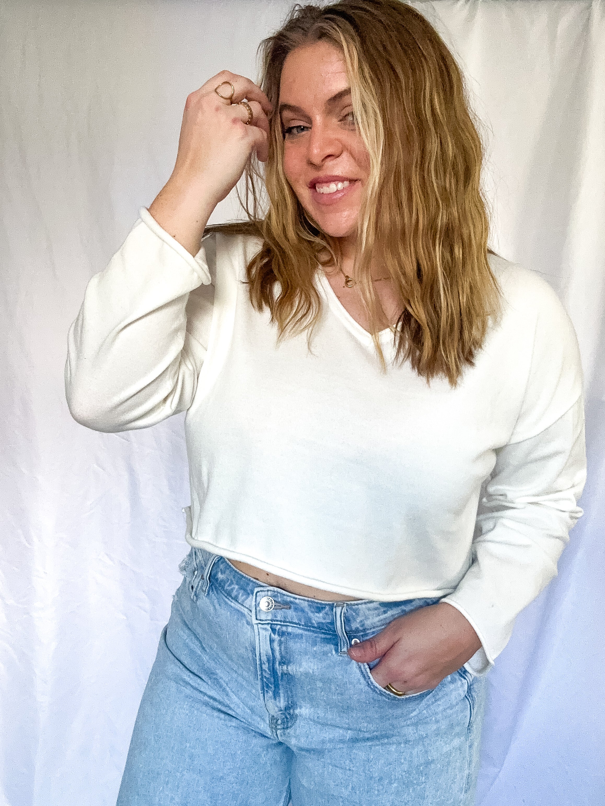 White cropped sweater with V-neckline and long sleeves, worn by a person.