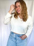 White cropped sweater with V-neckline and long sleeves, worn by a person.