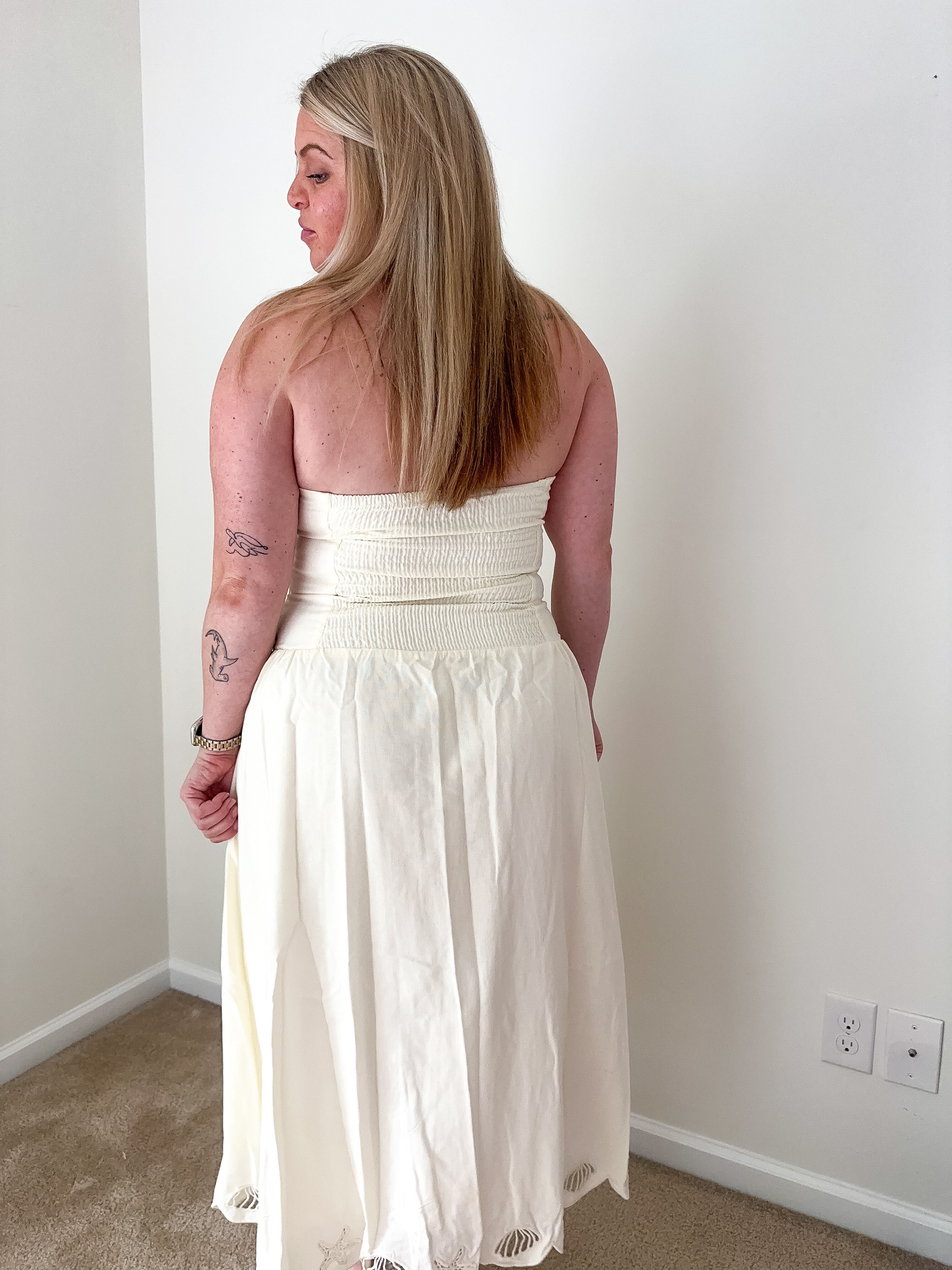 Woman wearing a white strapless dress standing against a plain wall.