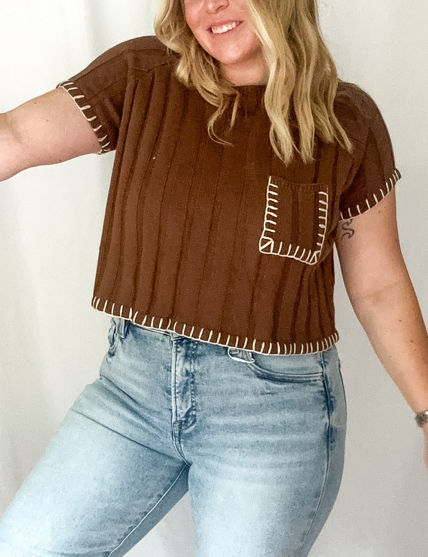 Person wearing a brown top with decorative sleeves and light blue jeans against a white background