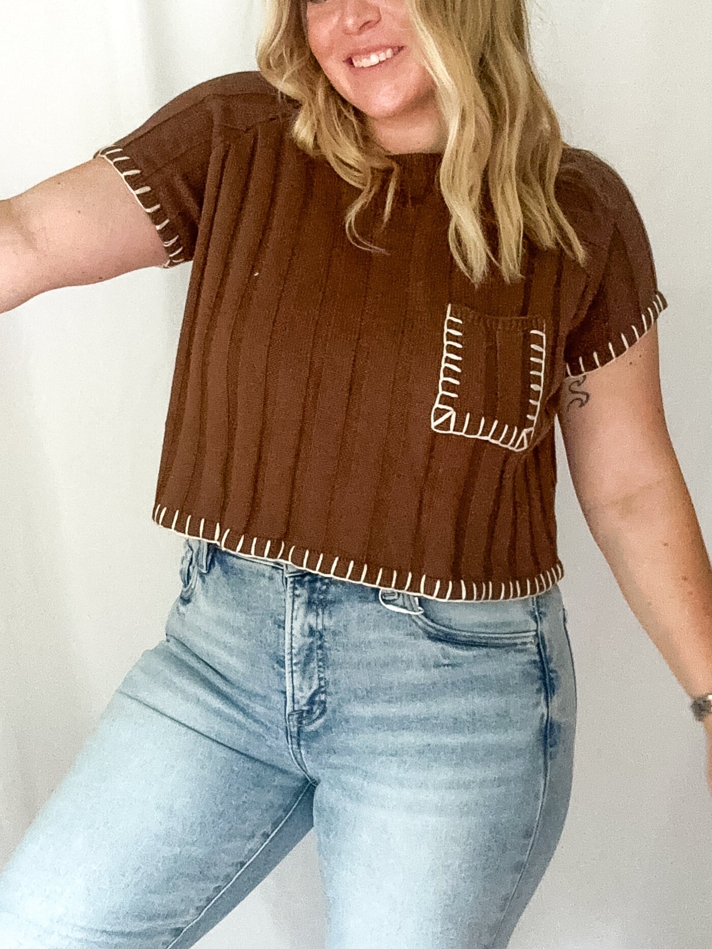 Person wearing a brown top with decorative sleeves and light blue jeans against a white background