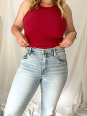 Person wearing a red tank top and light blue jeans against a plain background