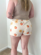 Person wearing a beige tank top and shorts with peach pattern against a white wall.