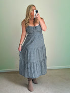A woman wearing a blue plaid midi dress with a scoop neckline and adjustable straps, featuring a tiered skirt and front tie.