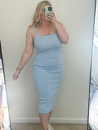 Person wearing a blue striped dress taking a mirror selfie in a room with a window and furniture.