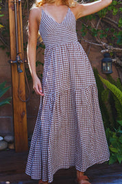 Woman wearing a checkered dress standing outdoors with plants and a wooden structure in the background