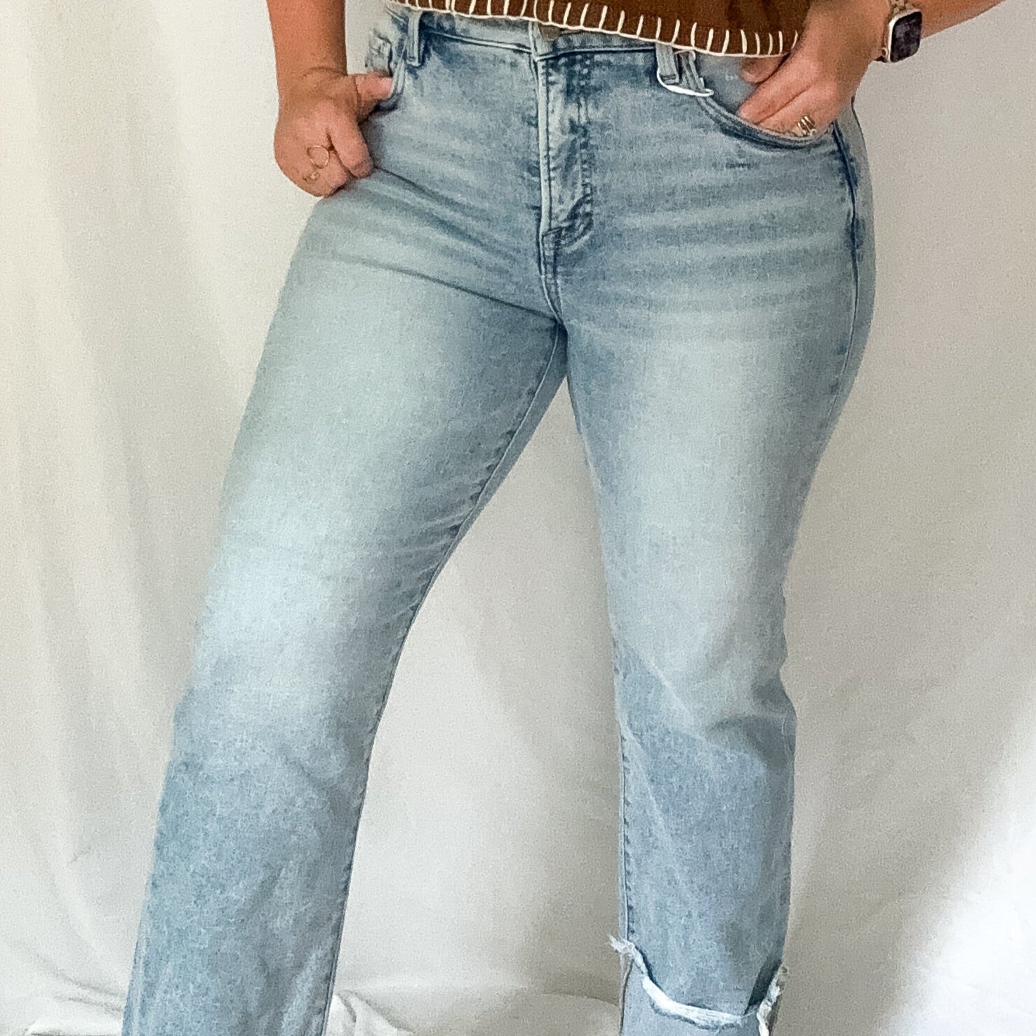 Woman wearing a brown top with fringe details and light blue jeans against a white background