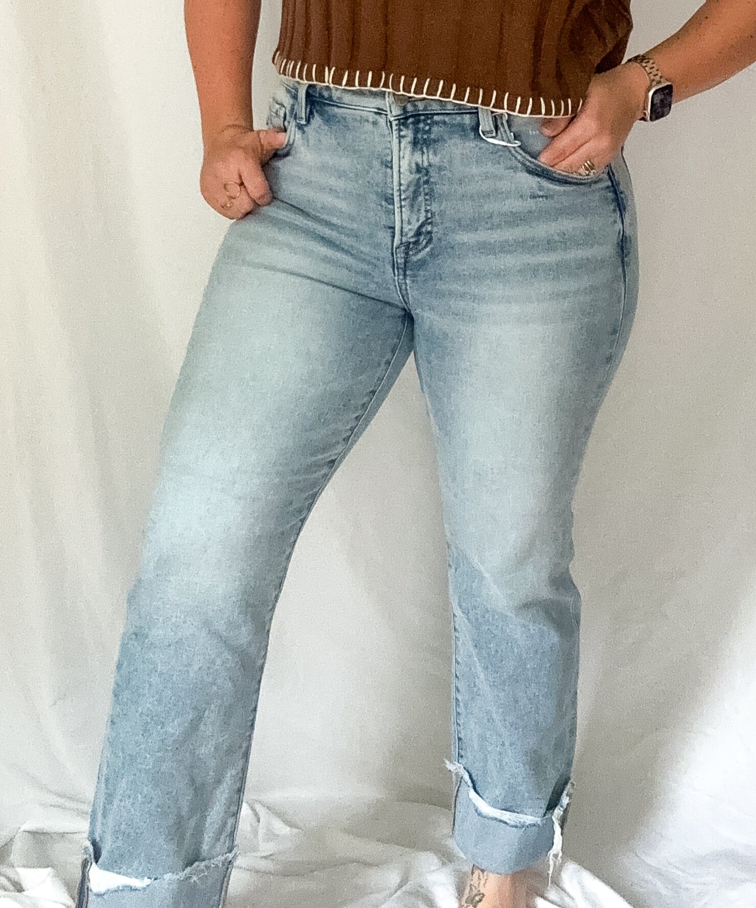 Woman wearing a brown top with fringe details and light blue jeans against a white background