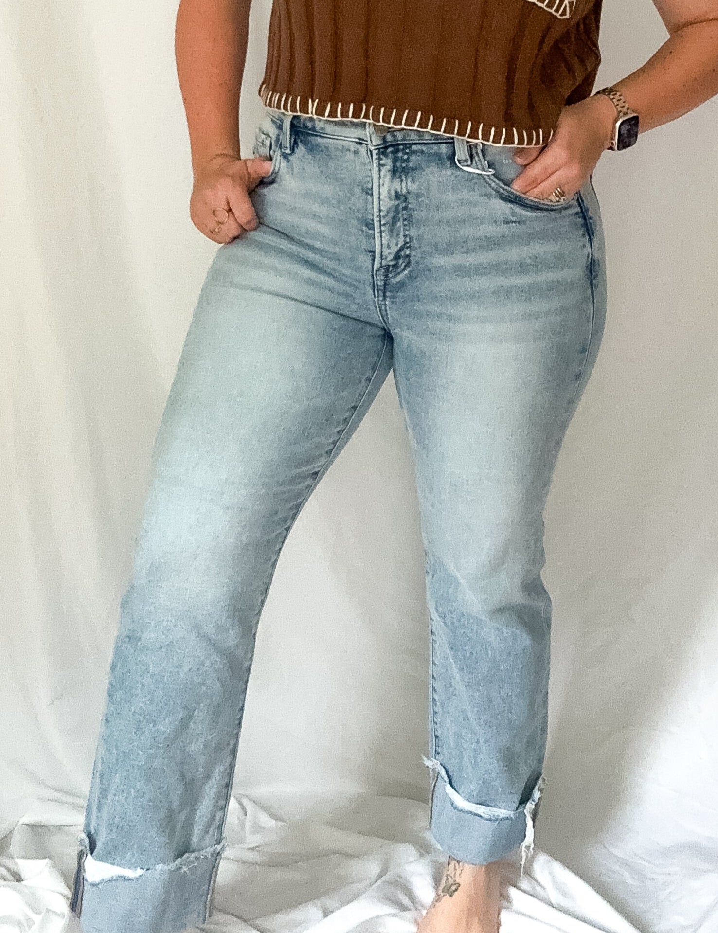 Woman wearing a brown top with fringe details and light blue jeans against a white background