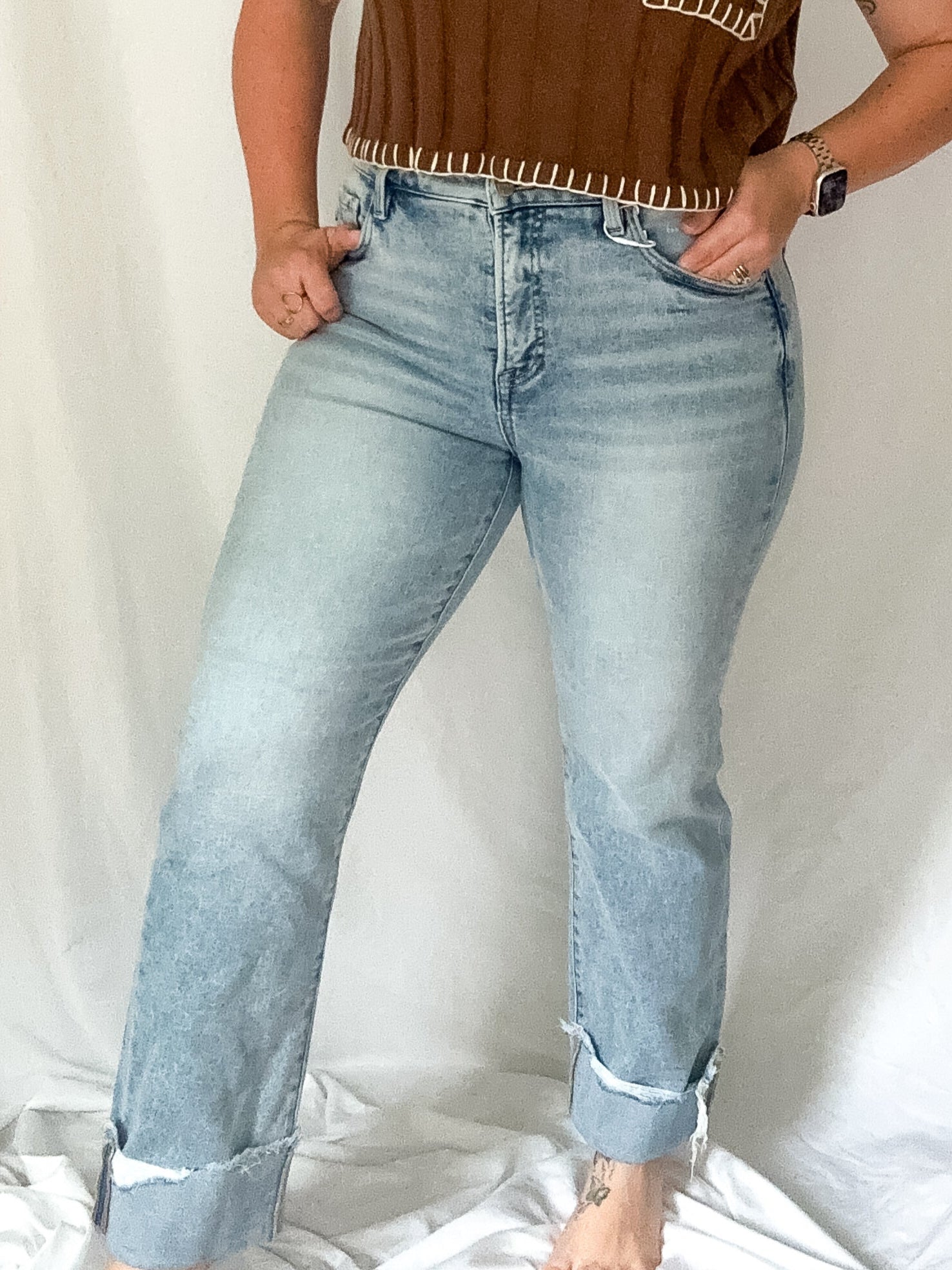 Woman wearing a brown top with fringe details and light blue jeans against a white background