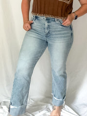 Woman wearing a brown top with fringe details and light blue jeans against a white background