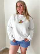 Person wearing a white sweatshirt with a logo and blue shorts indoors.