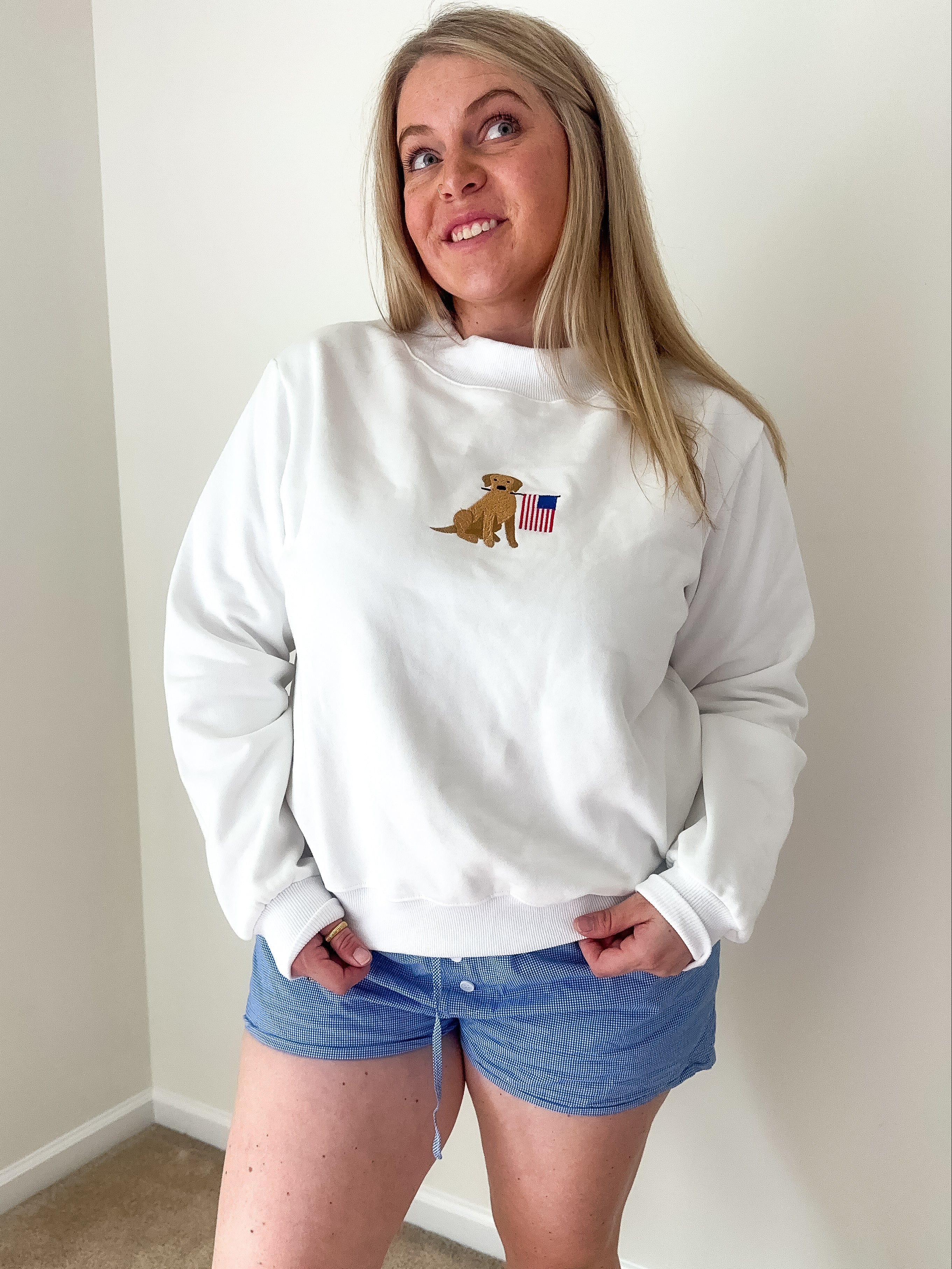 Person wearing a white sweatshirt with a logo and blue shorts indoors.