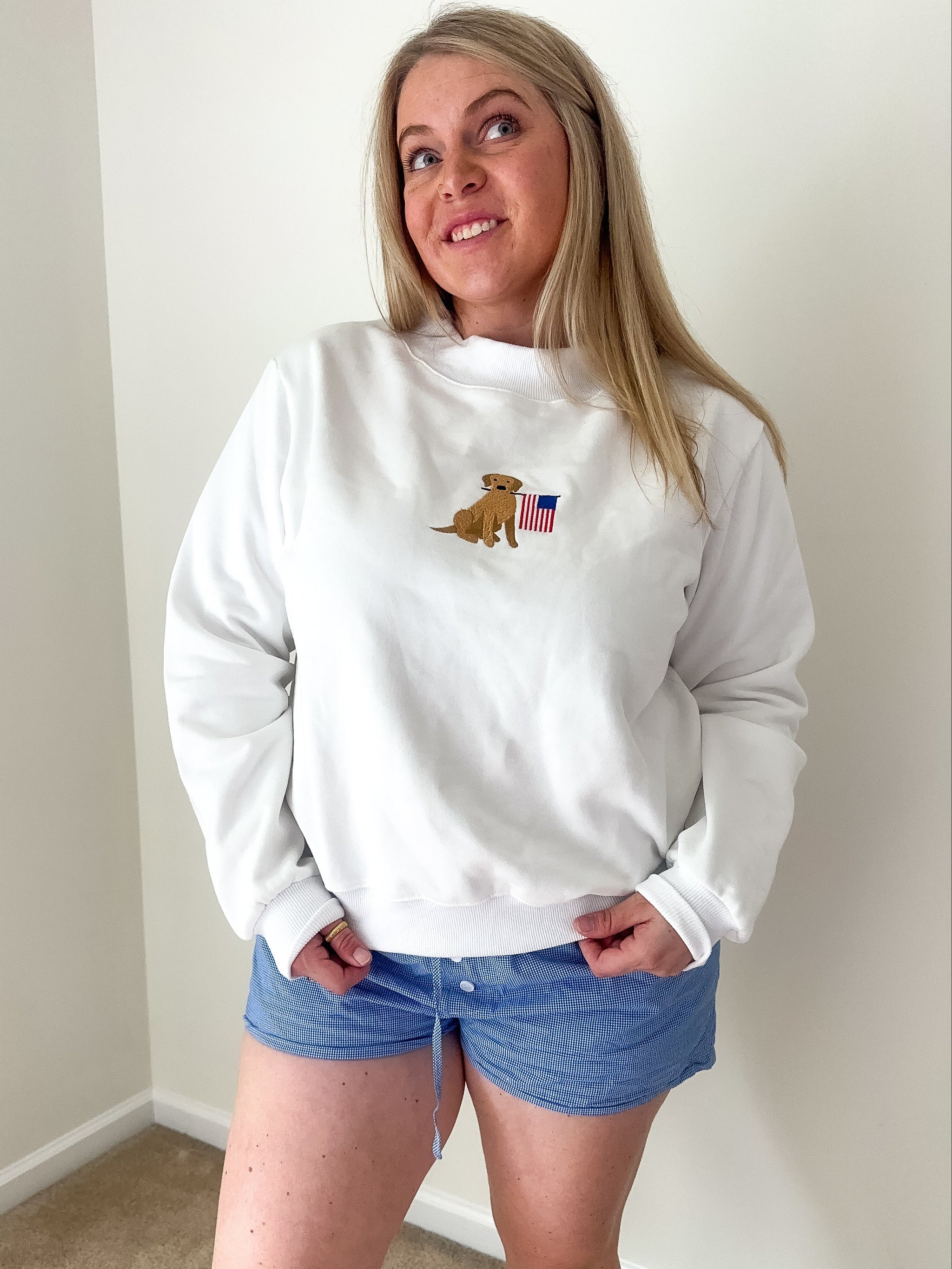 Person wearing a white sweatshirt with a logo and blue shorts indoors.