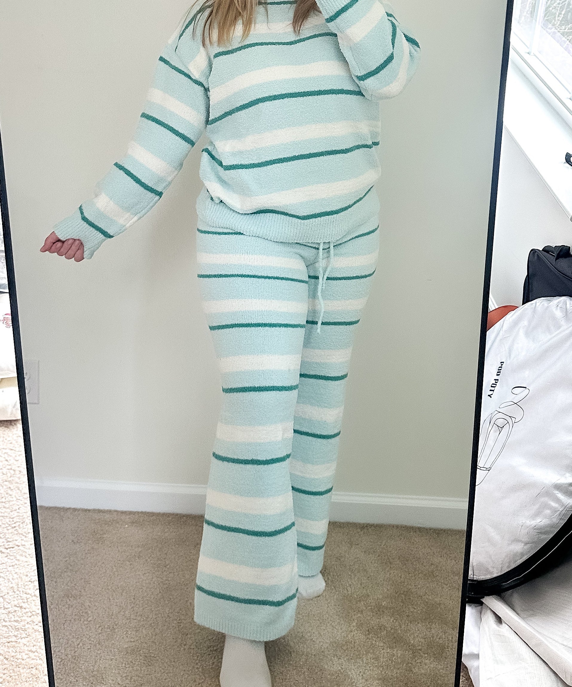 Person wearing a striped outfit taking a mirror selfie in a room with a large mirror.