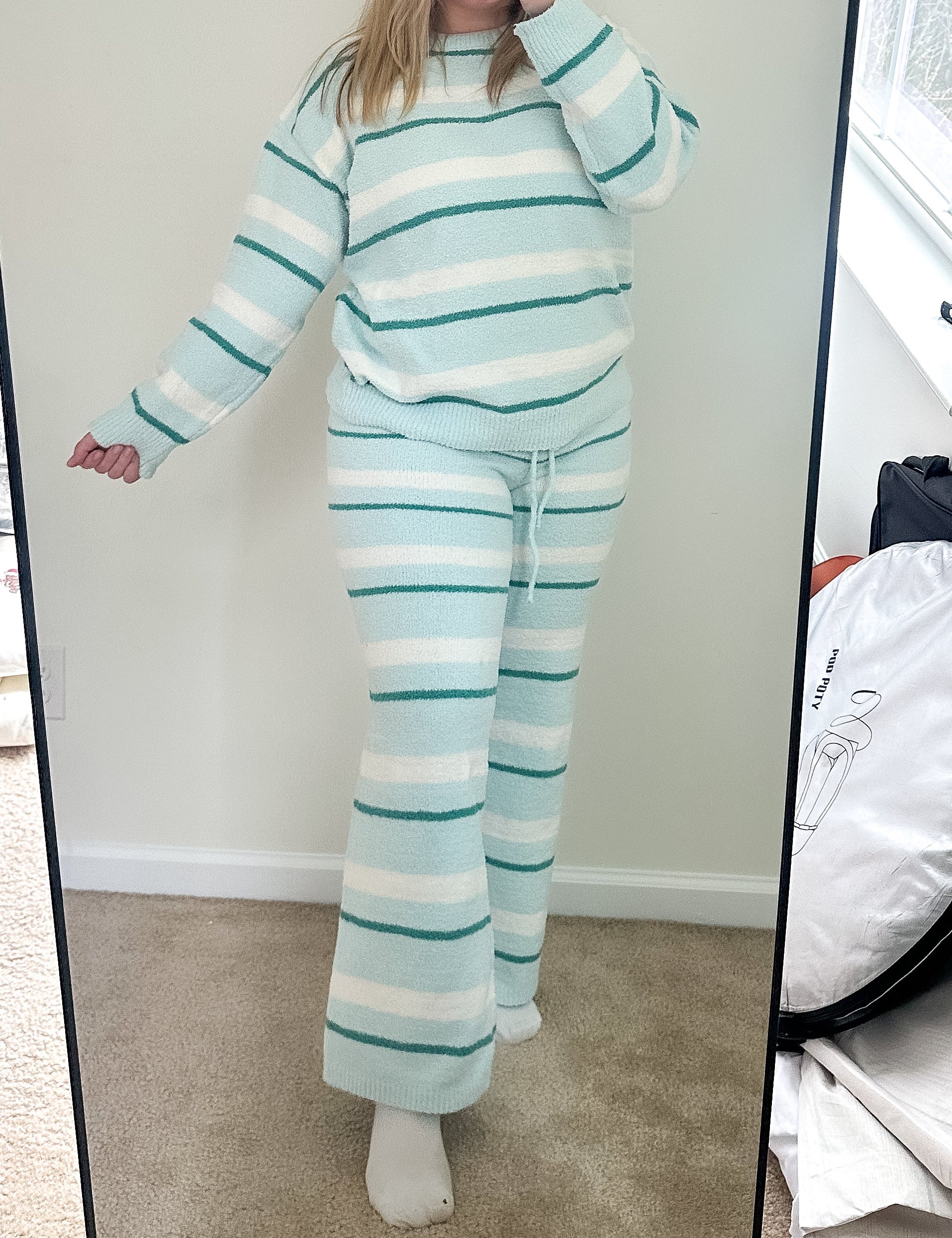 Person wearing a striped outfit taking a mirror selfie in a room with a large mirror.