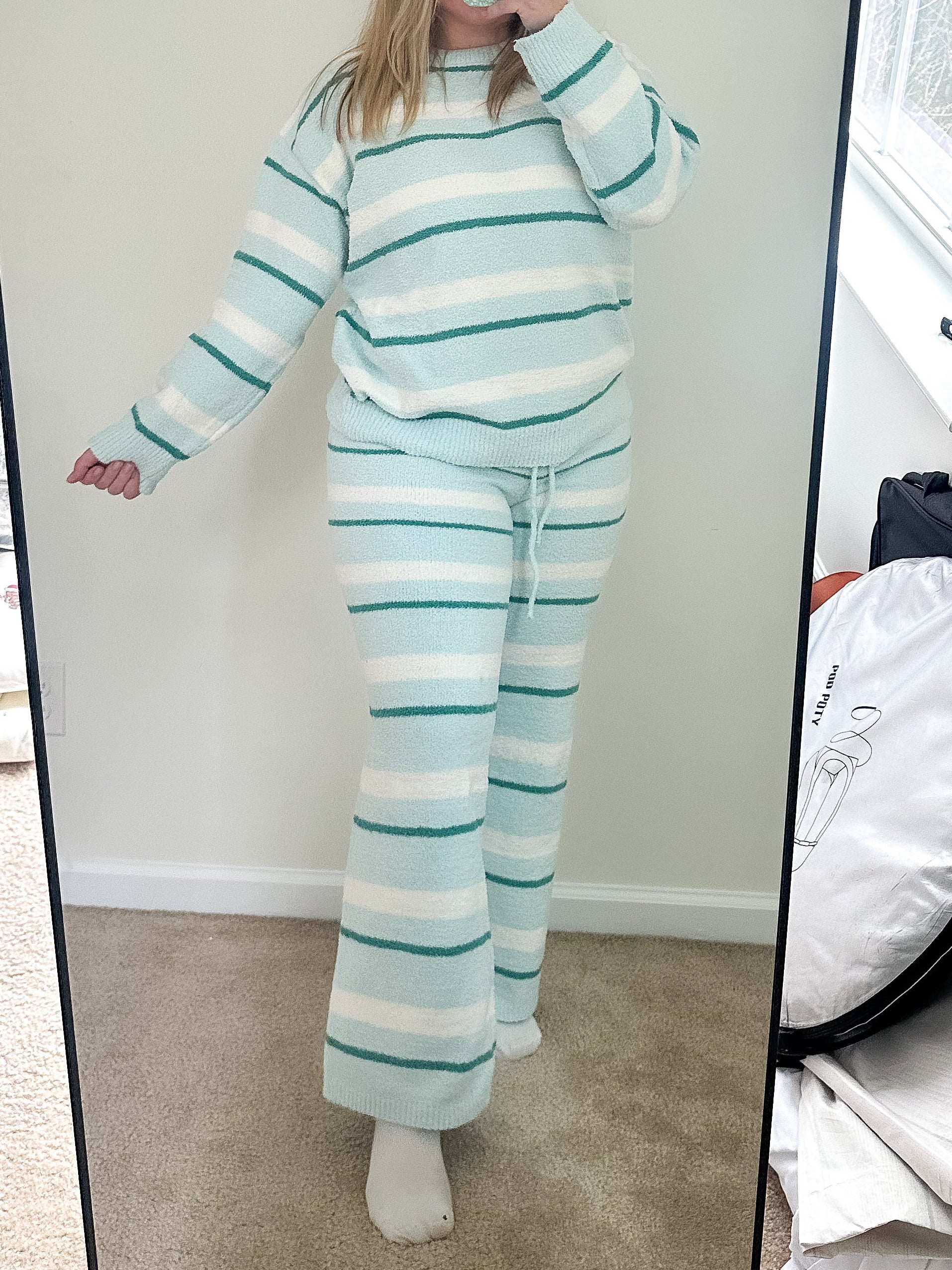 Person wearing a striped outfit taking a mirror selfie in a room with a large mirror.