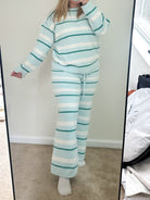 Person wearing a striped outfit taking a mirror selfie in a room with a large mirror.