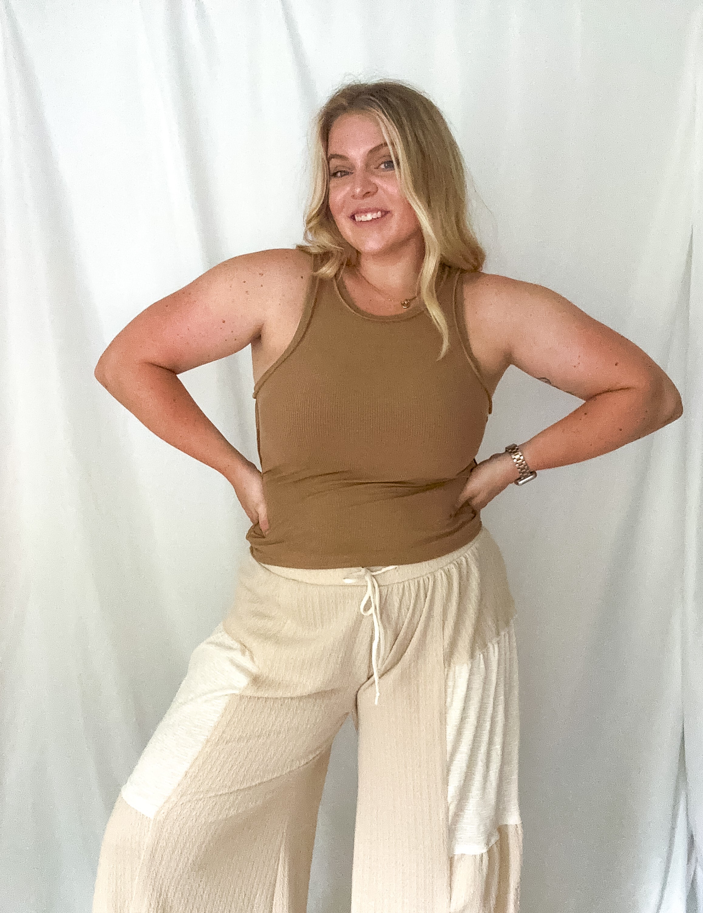 Woman wearing a brown tank top and beige pants against a white background