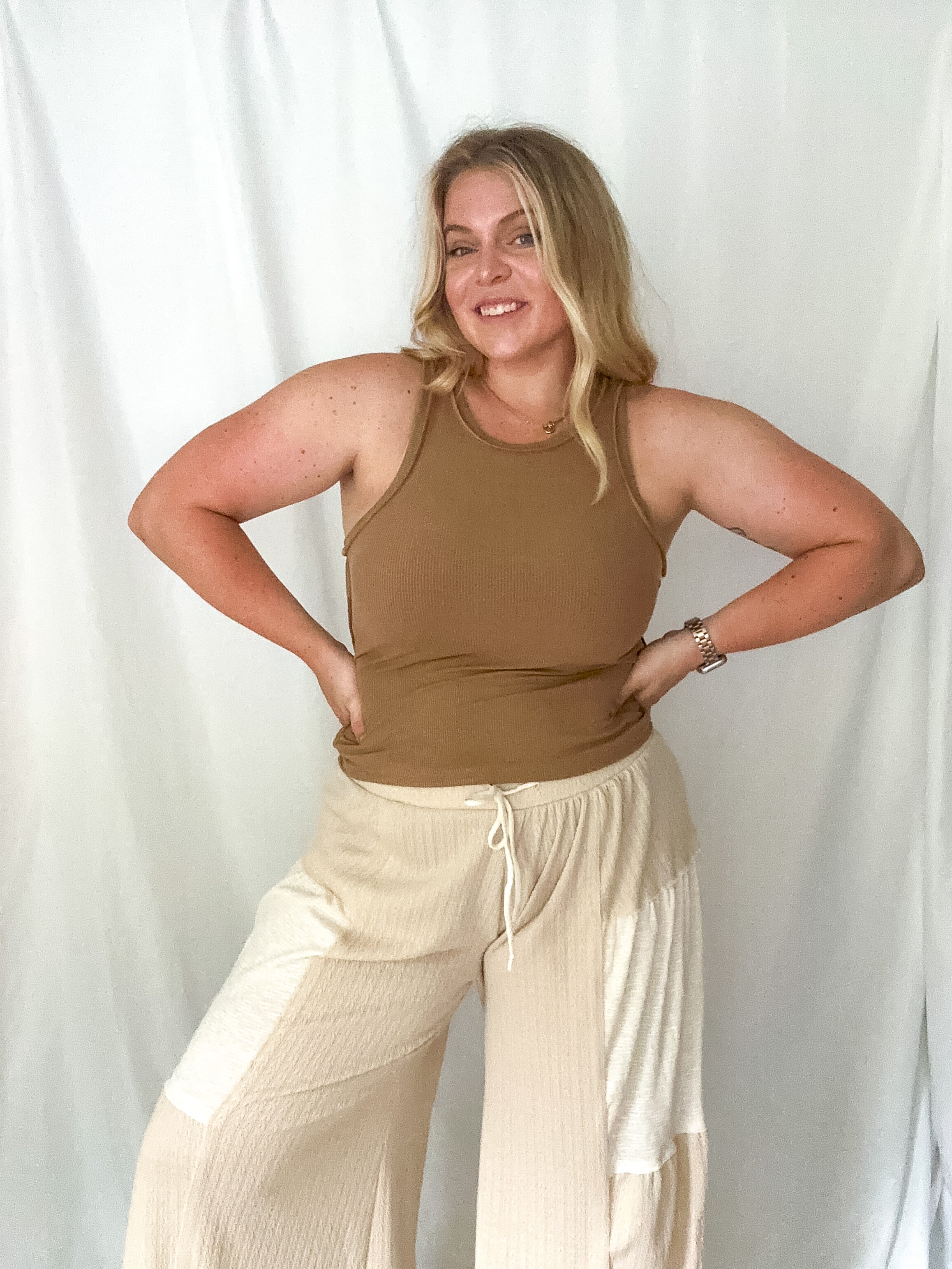 Woman wearing a brown tank top and beige pants against a white background