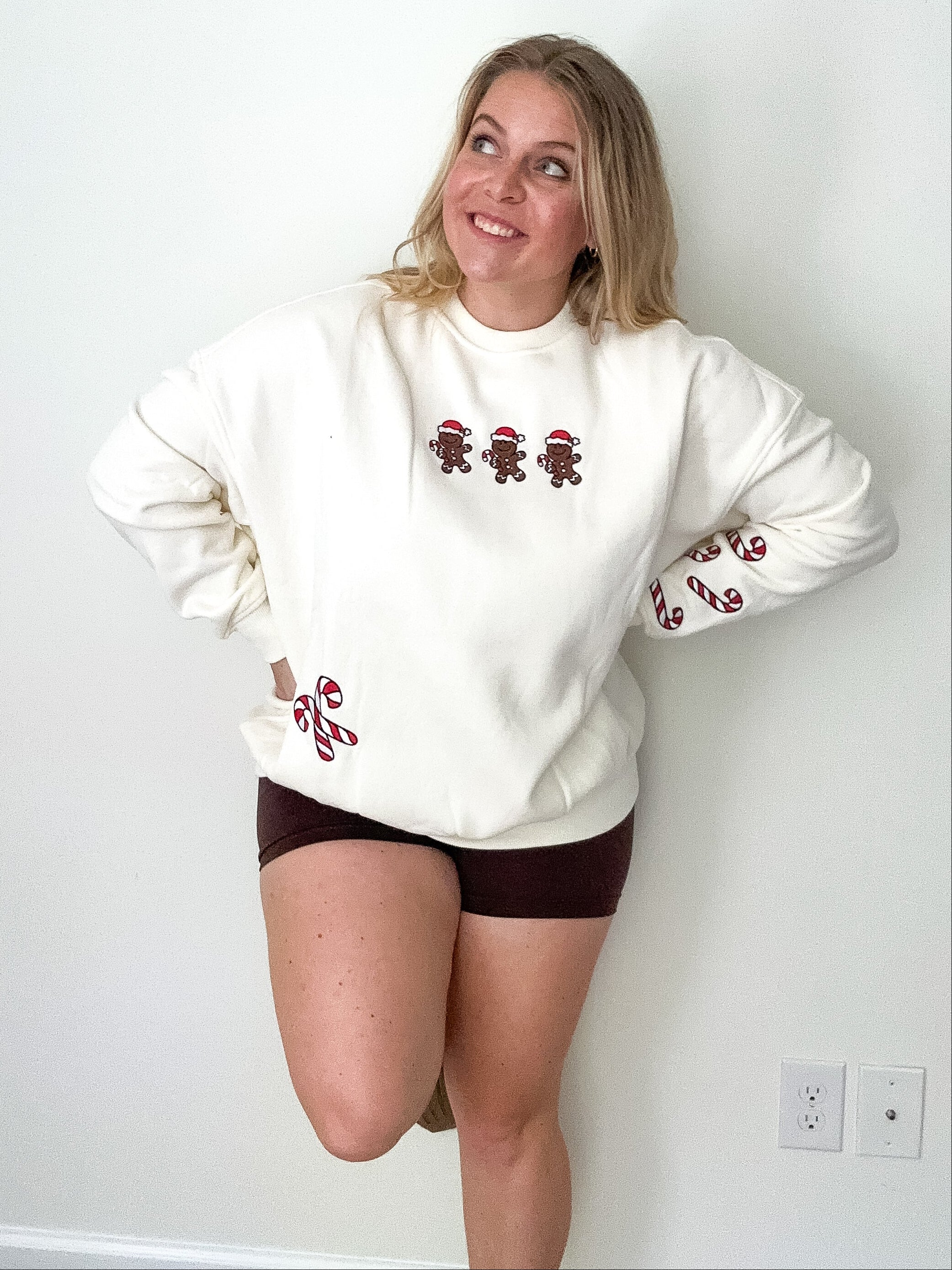 Person wearing a white sweatshirt with gingerbread design against a plain wall.