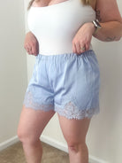 Person wearing a white top and light blue shorts with lace trim against a plain wall.