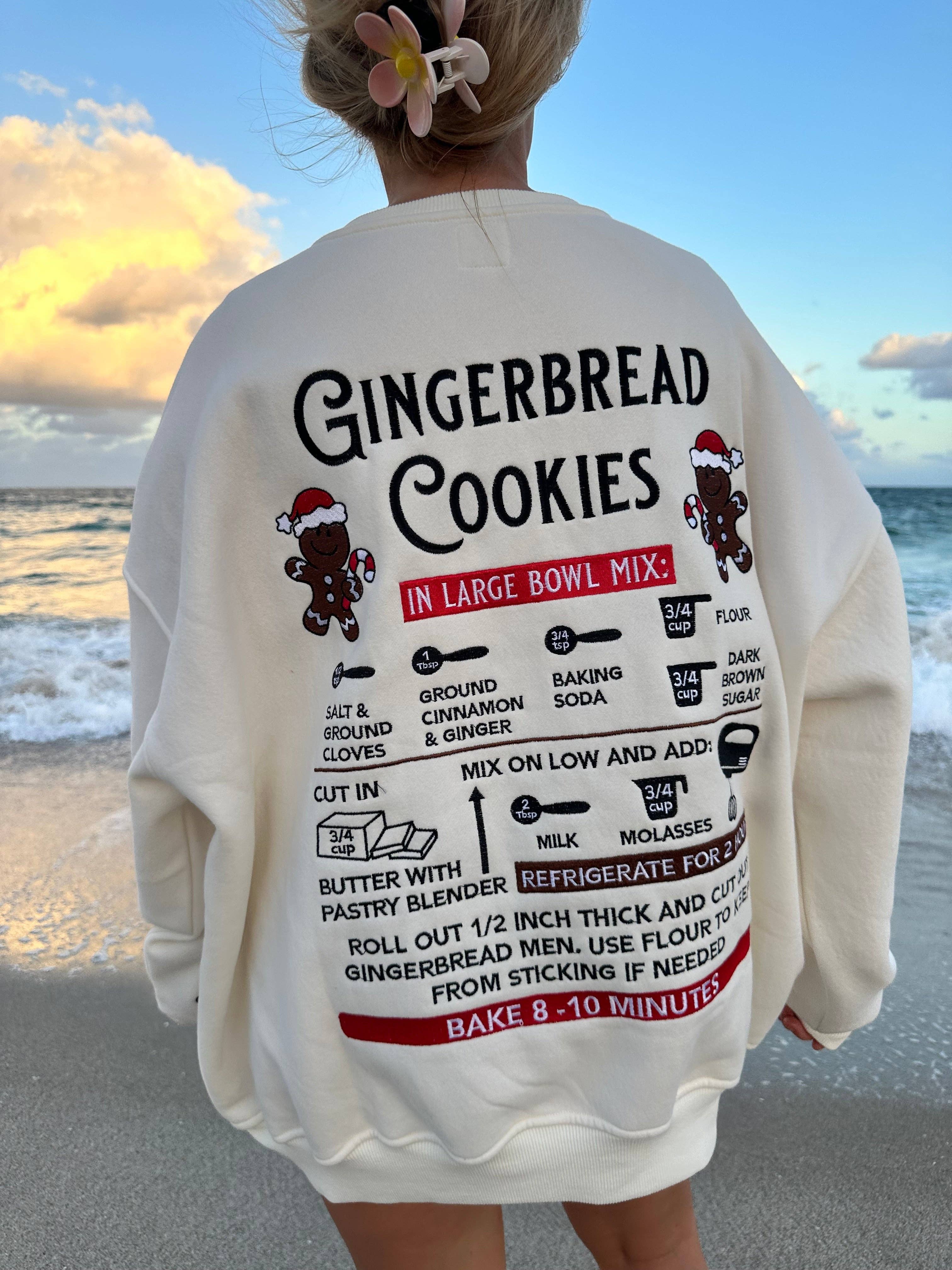 Person wearing a sweater with a gingerbread cookies recipe design at the beach.