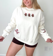 Woman wearing a white sweatshirt with red designs, standing against a plain wall.