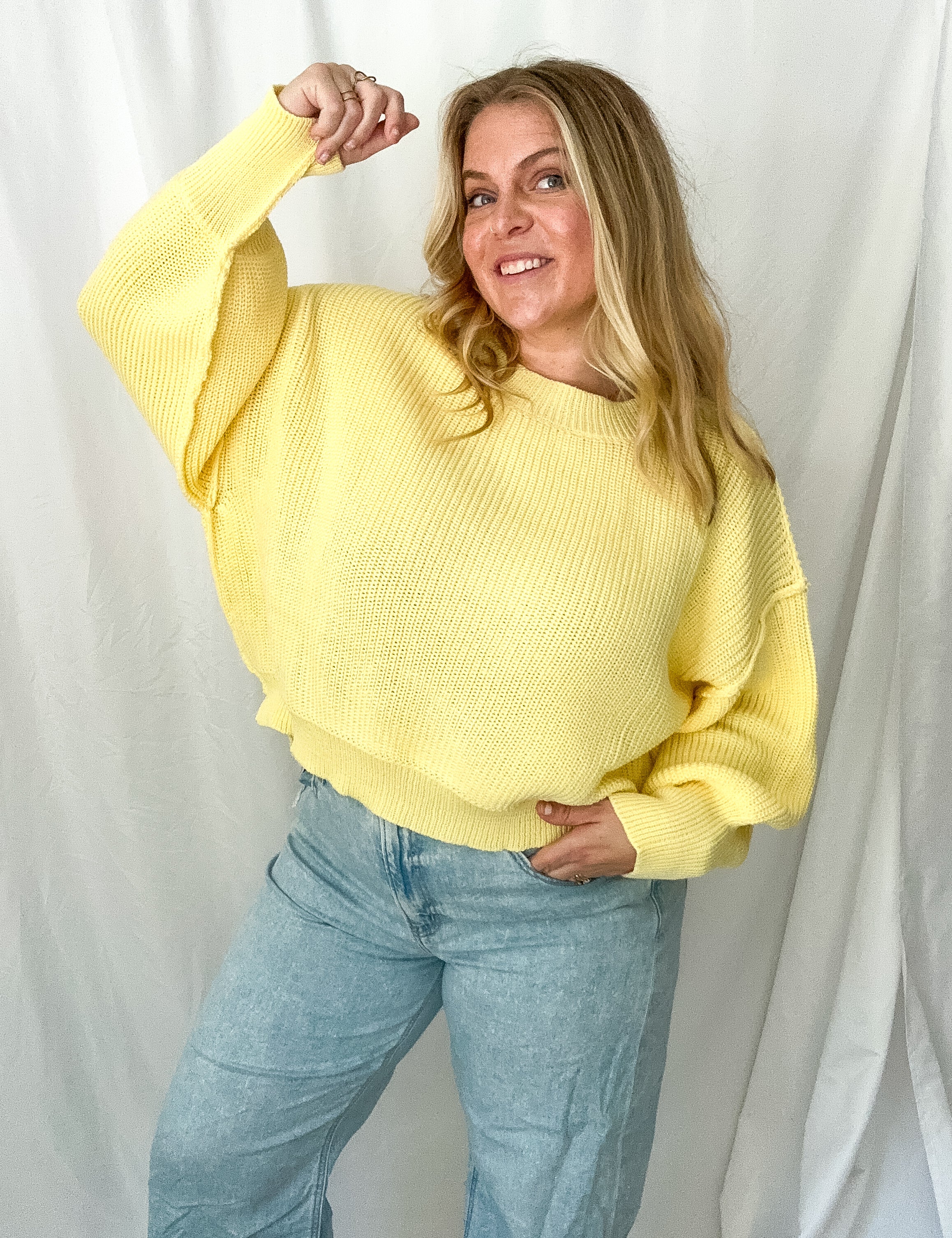 Person wearing a yellow sweater and light blue jeans against a white background