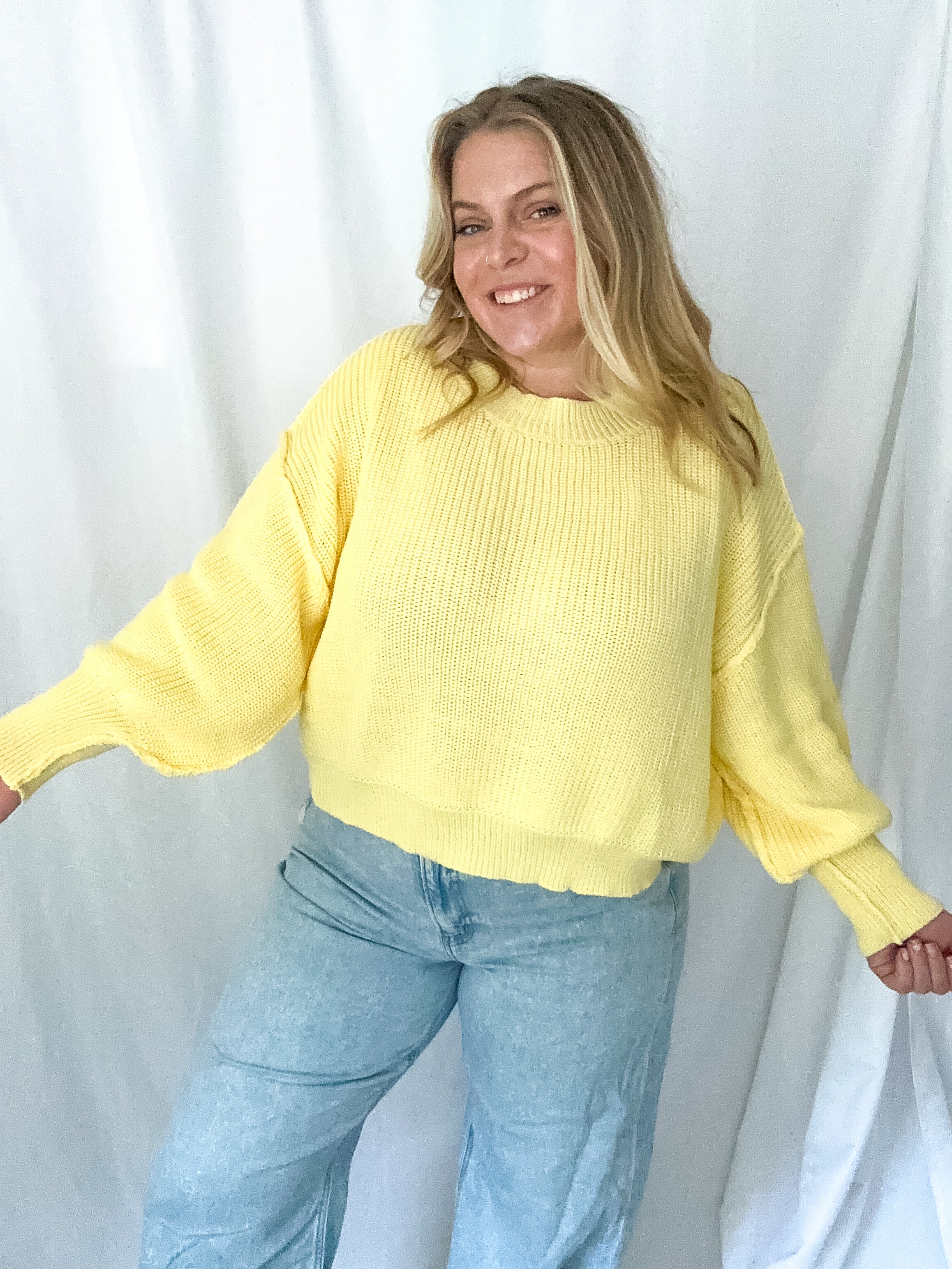 Person wearing a yellow sweater and blue jeans against a white background