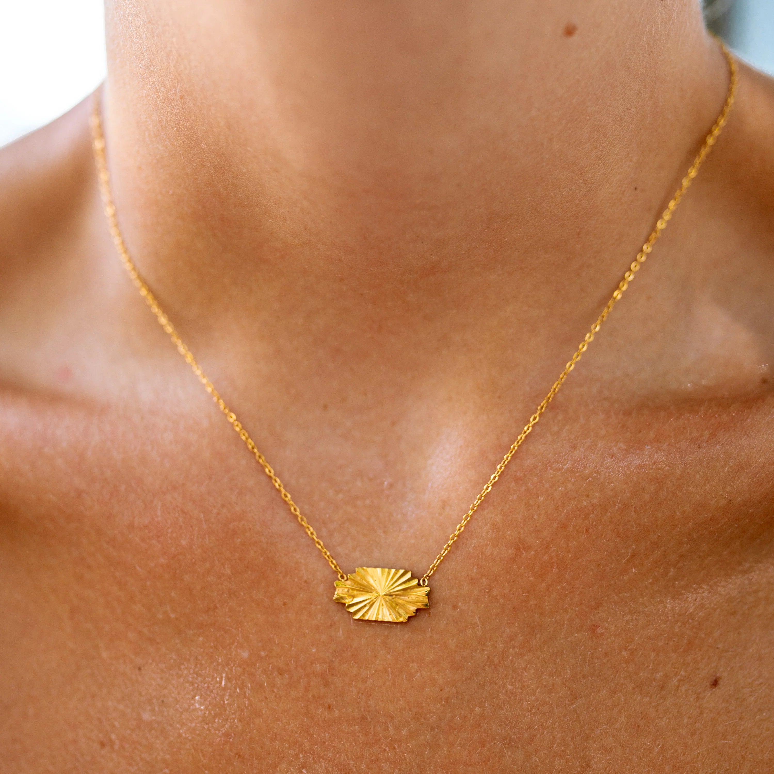 Gold necklace with a leaf pendant on a person's neck