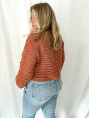 Person wearing a brown knitted sweater and light blue jeans against a white background