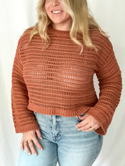 Woman wearing a brown knitted sweater and light blue jeans against a white background