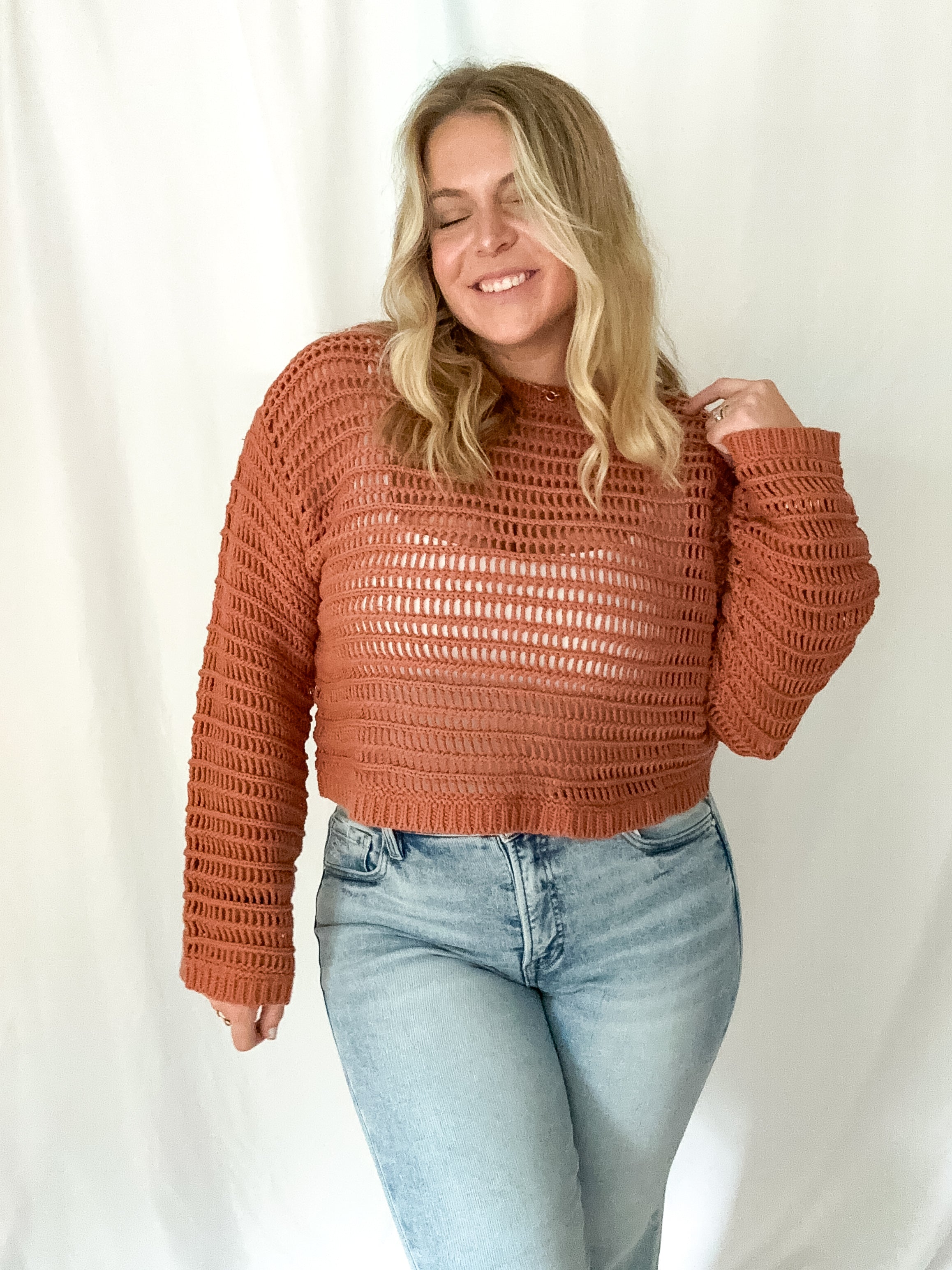 Woman wearing a brown textured sweater and light blue jeans against a white background