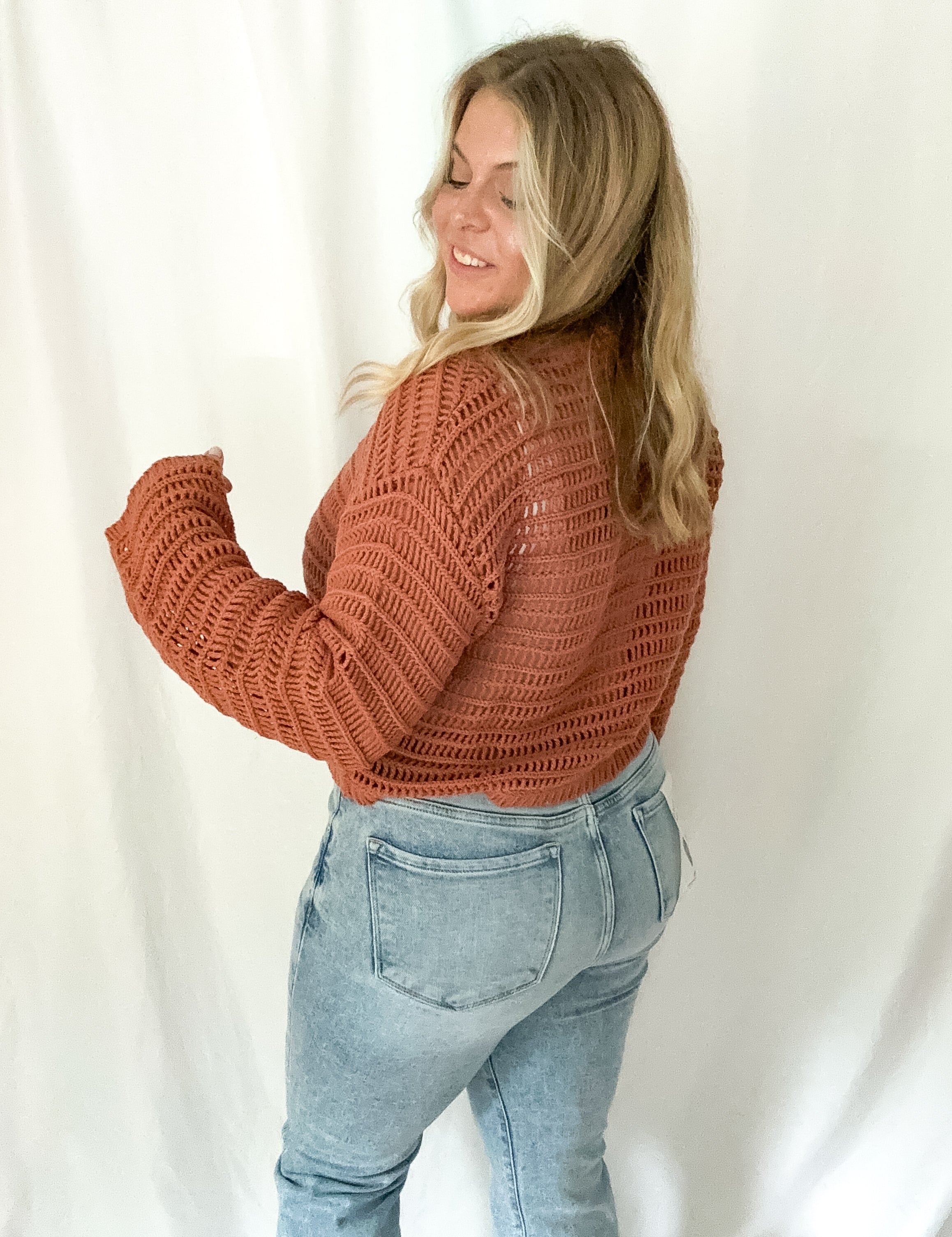 Woman wearing a brown knitted sweater and light blue jeans against a white background