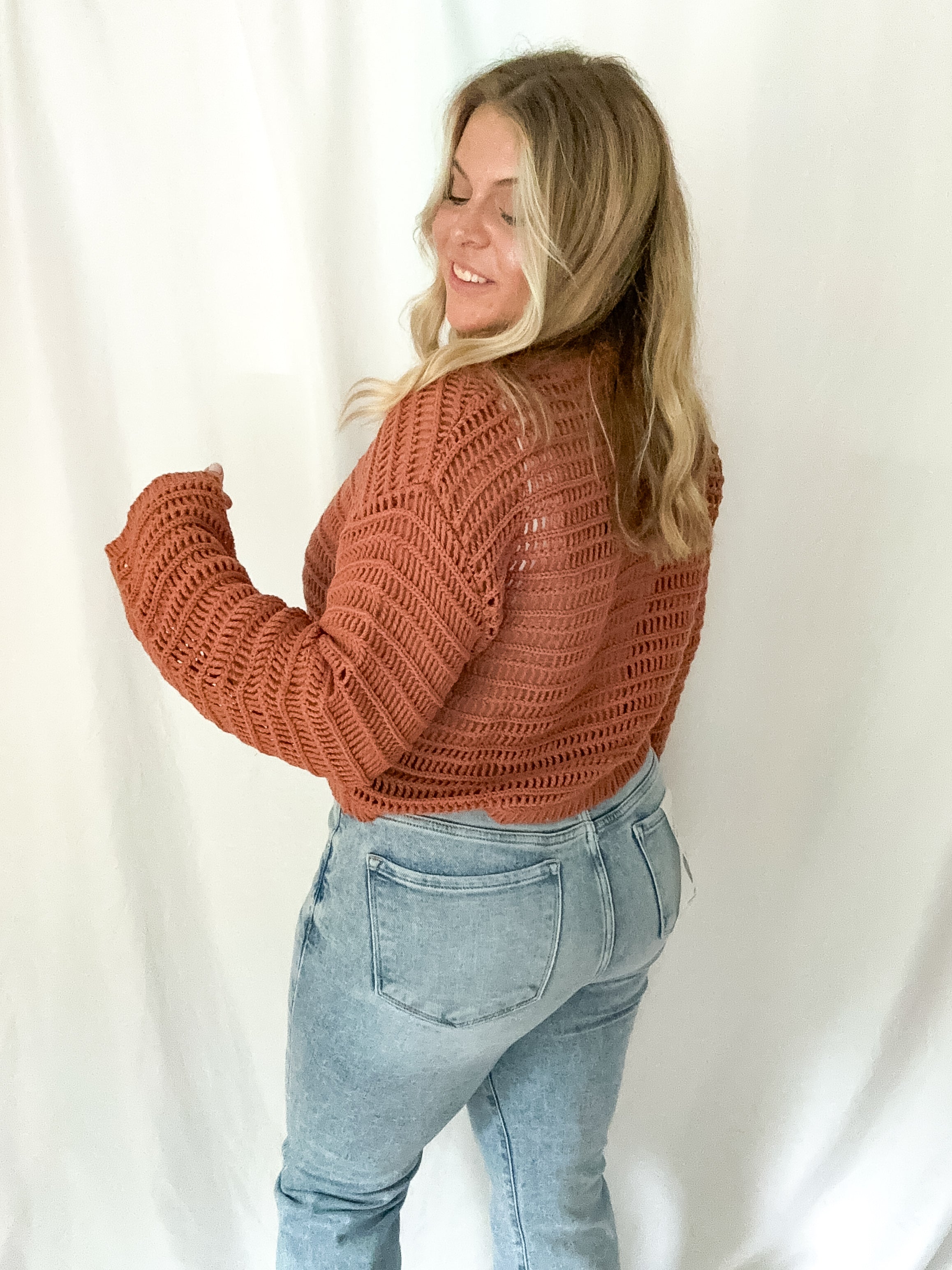Woman wearing a brown knitted sweater and light blue jeans against a white background