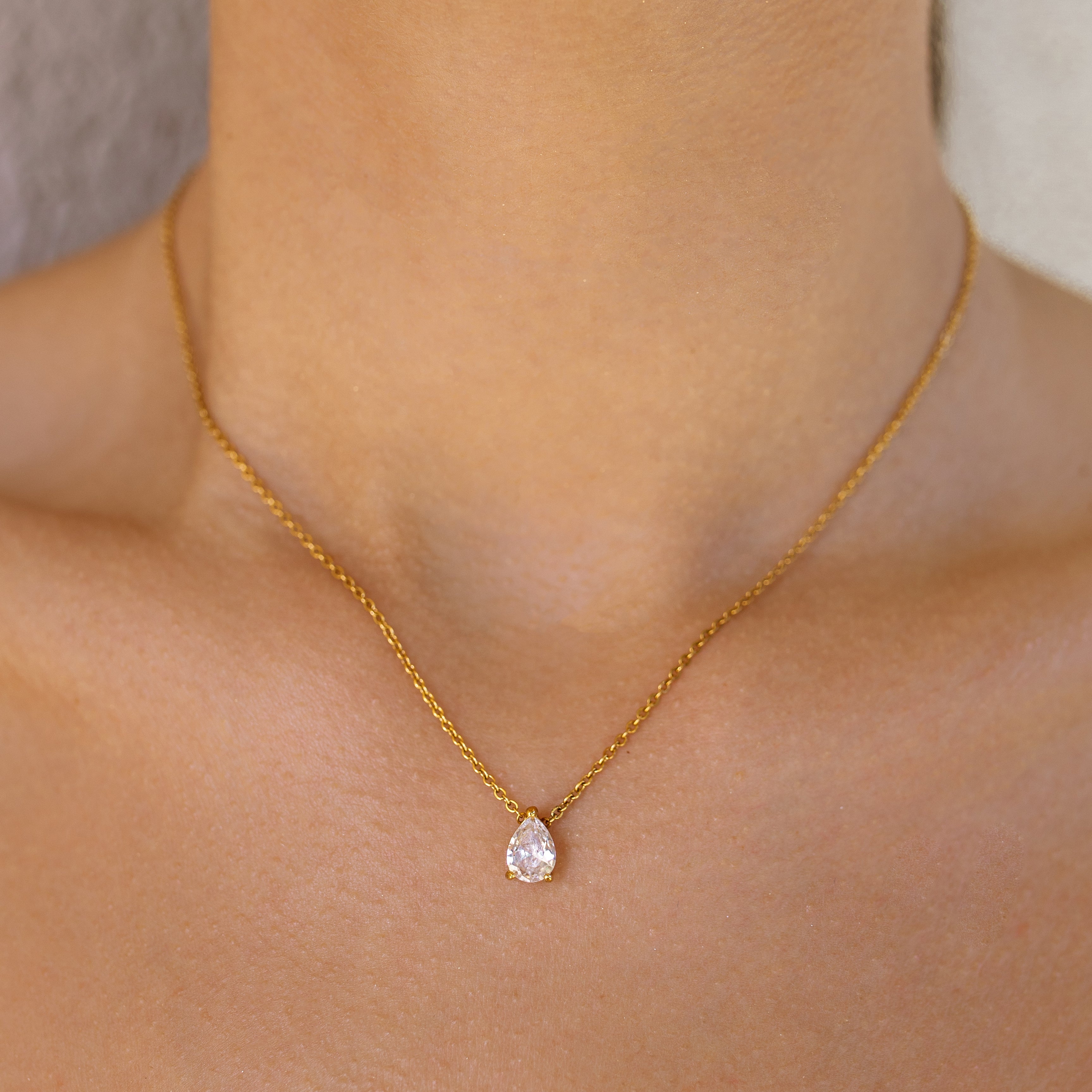 Gold necklace with a teardrop-shaped pendant on a person's neck