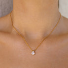 Gold necklace with a teardrop-shaped pendant on a person's neck
