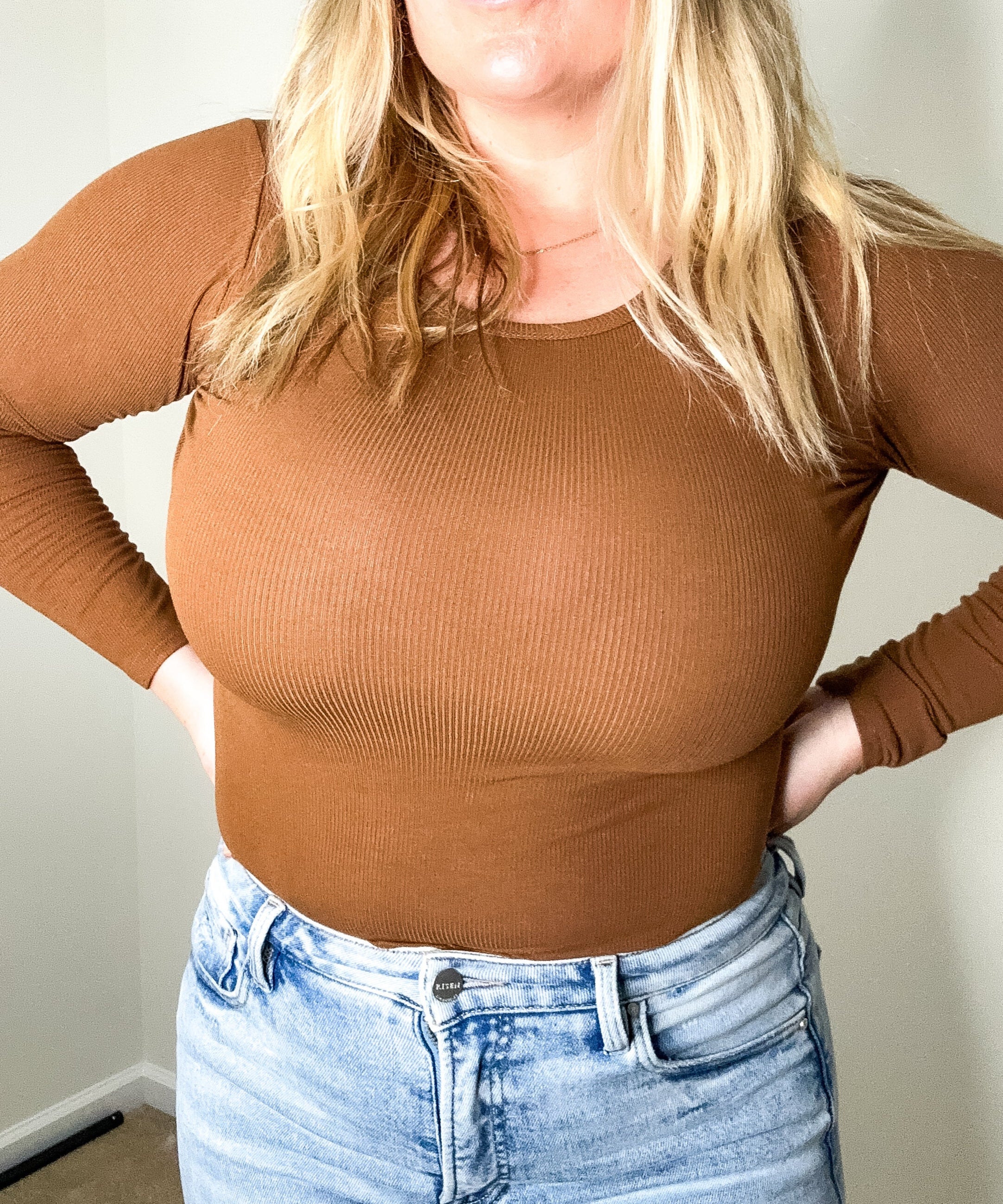 Person wearing a brown ribbed long-sleeve top and light blue jeans indoors.