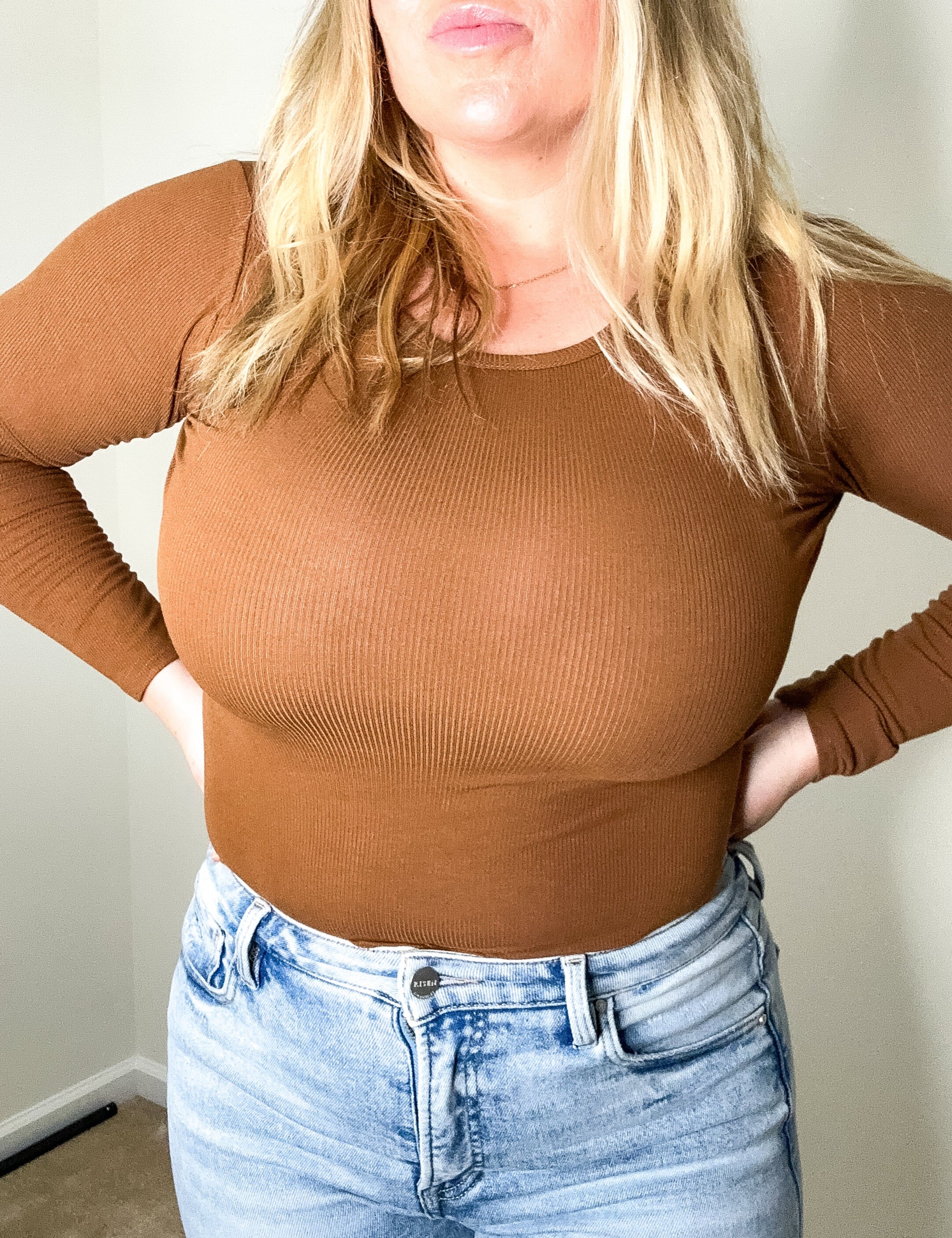 Person wearing a brown ribbed long-sleeve top and light blue jeans indoors.