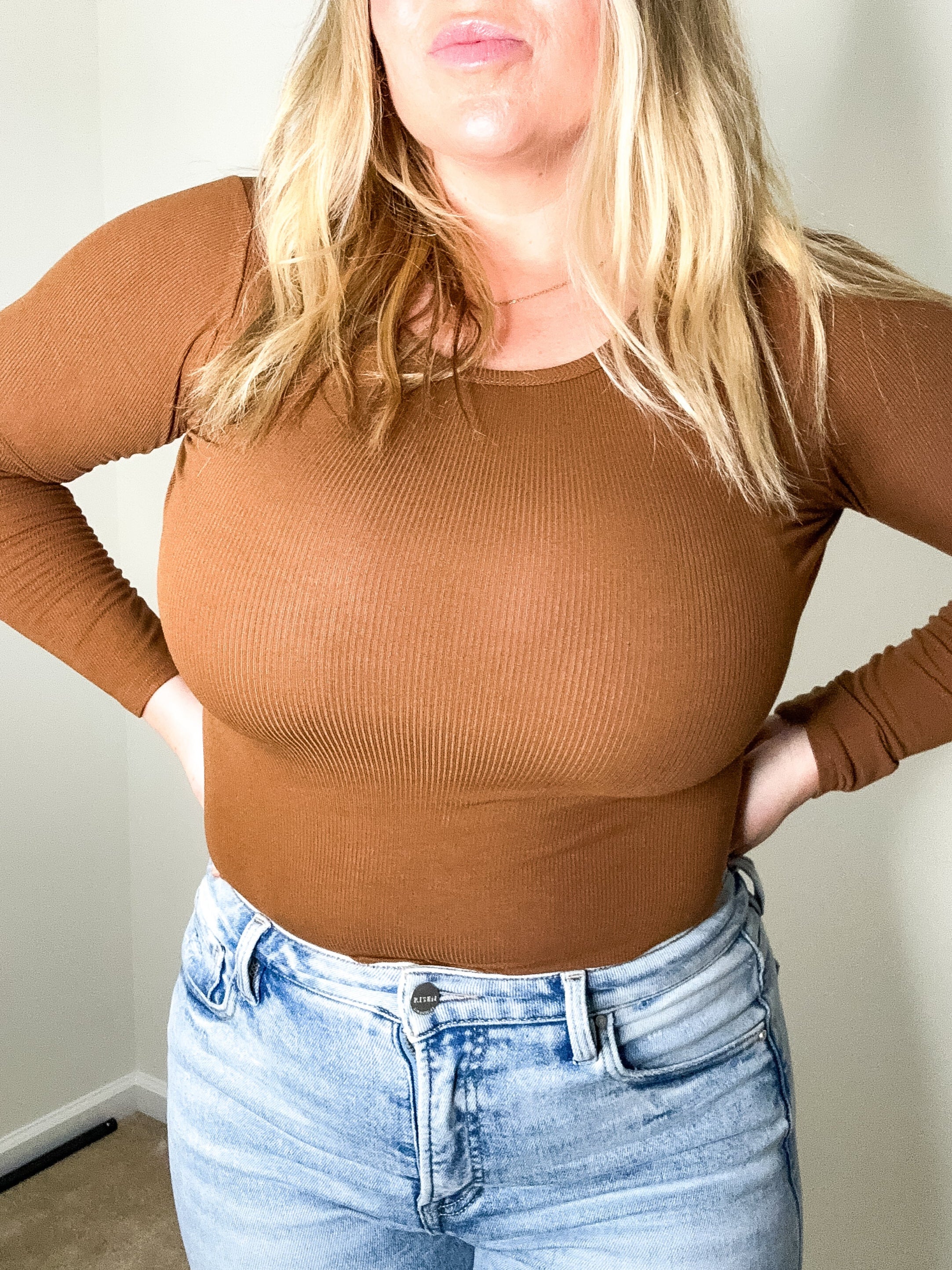 Person wearing a brown ribbed long-sleeve top and light blue jeans indoors.