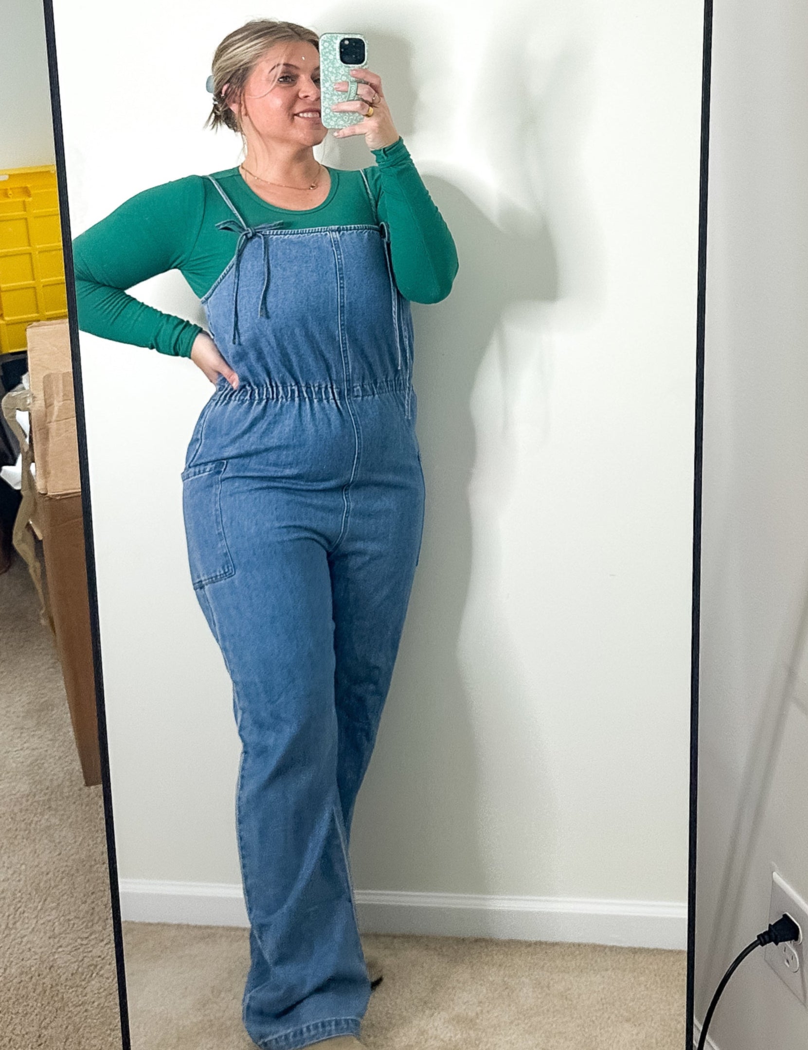 Person wearing a blue jumpsuit taking a mirror selfie in a room.