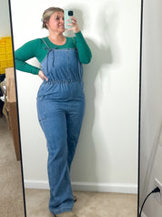 Person wearing a blue jumpsuit taking a mirror selfie in a room.