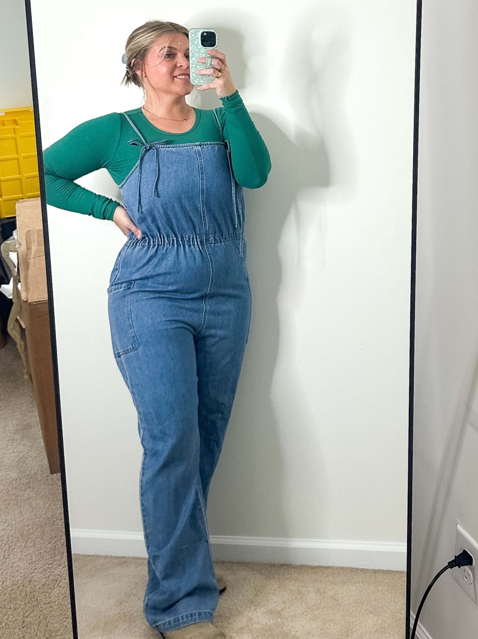 Person wearing a blue jumpsuit taking a mirror selfie in a room.